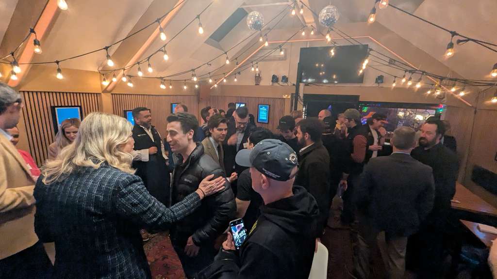 Grupo de asistentes conversando bajo luces colgantes en el salón trasero de PubKey durante un evento Bitcoin en Nueva York