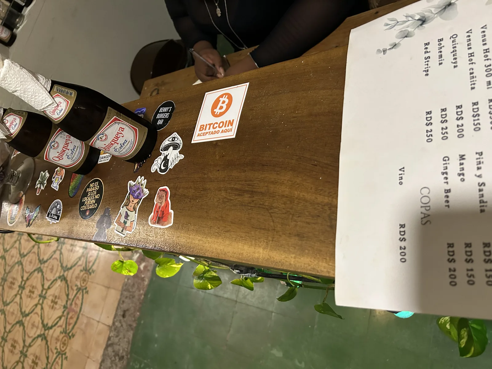 Menú del lugar junto a una calcomanía de Bitcoin Accepted Here sobre la mesa