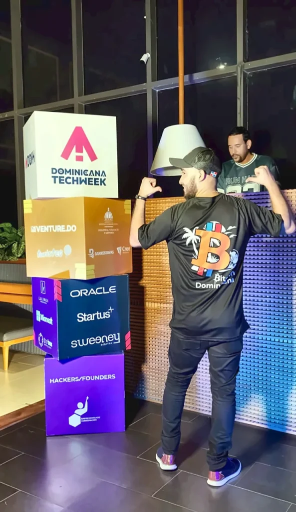 Asistente con la camiseta de Bitcoin Dominicana frente a los cubos de patrocinadores de Dominicana Tech Week 2026.