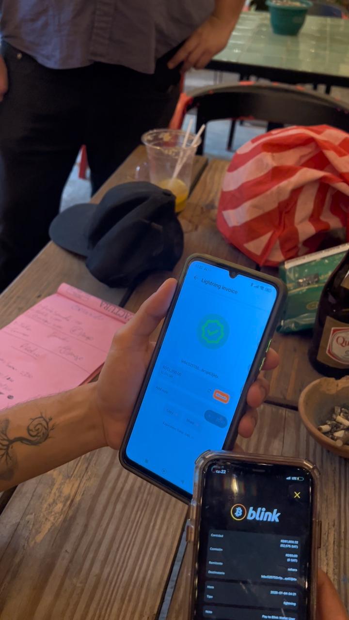Confirmación del pago con Bitcoin por Lightning en la wallet Blink junto a la cuenta en papel, The Perpetual Lab, Zona Colonial