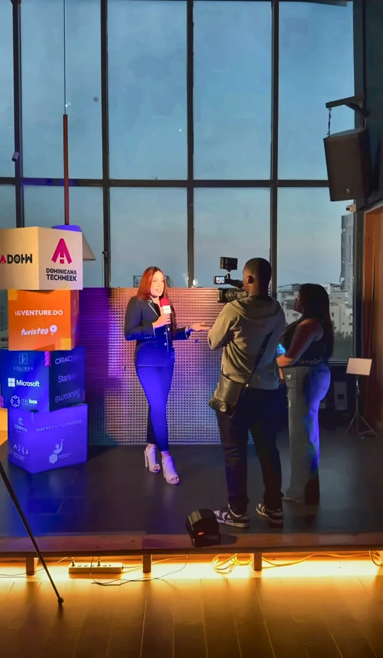 Una organizadora es entrevistada ante cámara junto a los cubos de patrocinadores de Dominicana Tech Week.