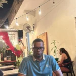 Carlos Gutiérrez, de Quisqueya Project (izquierda), conversa sobre Bitcoin con dos participantes en el patio de The Perpetual Lab, en la Zona Colonial de Santo Domingo, de noche y bajo luces colgantes